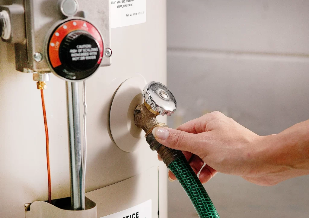 Male plumber flushing a residential water heater to improve performance and extend its lifespan for NWA C&S Plumbing.