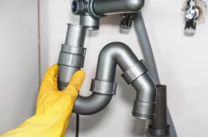 Gloved plumber holding a sink drain pipe section while diagnosing a slow-draining sink for NWA C&S Plumbing