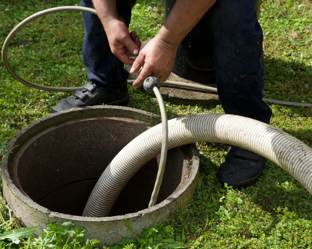 A professional plumber performing a heavy-duty drain cleaning service in Fayetteville, AR, feeding a high-pressure line and a large suction hose directly into an outdoor sewer cleanout manhole.