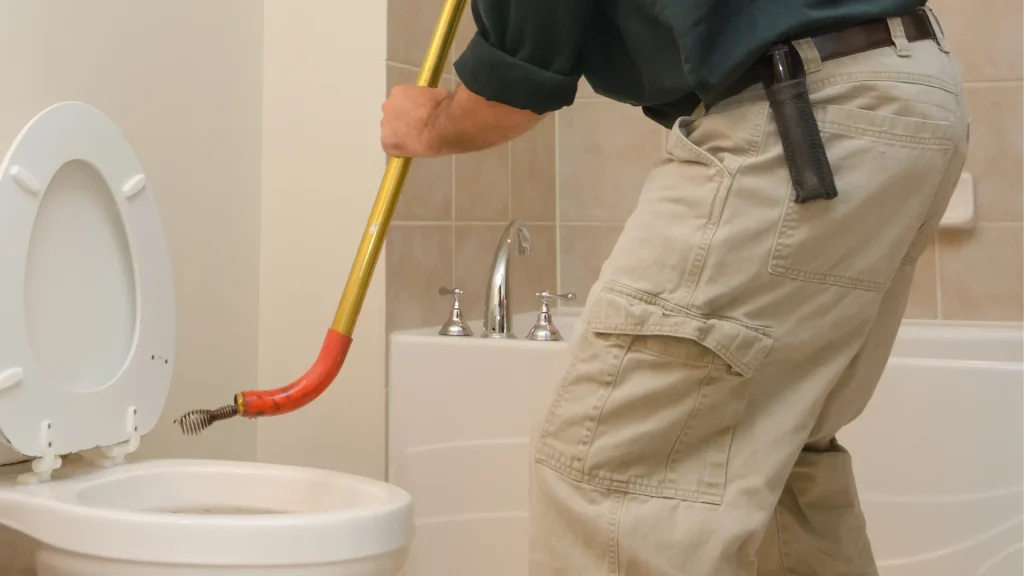 Plumber using a toilet auger to clear a recurring toilet clog